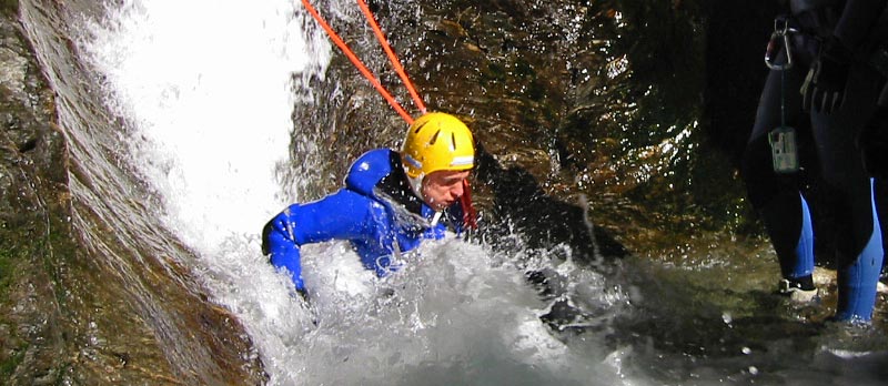 Mann mit Helm und Trockenanzug springt einen Wasserfall runter ins Wasser.