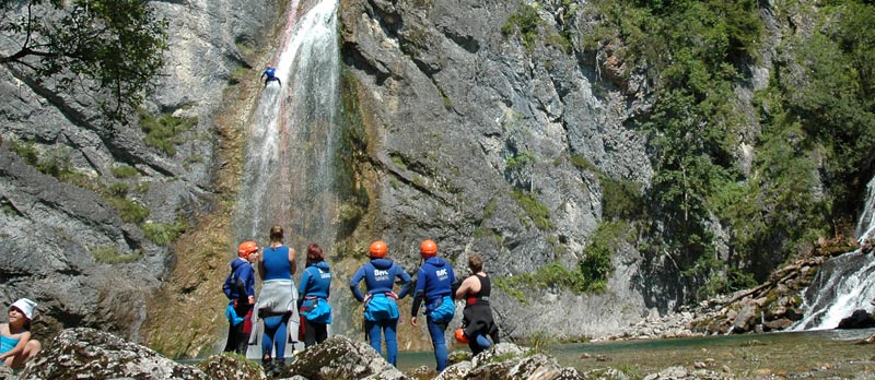 Gruppe von Menschen steht in Trockenanzügen vor einem großen Wasserfall in der Natur.